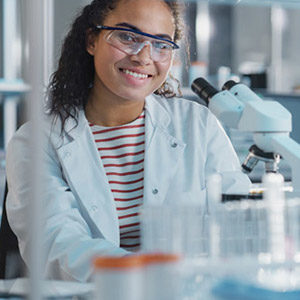 Woman wearing lab coat and goggles in front of a microscope